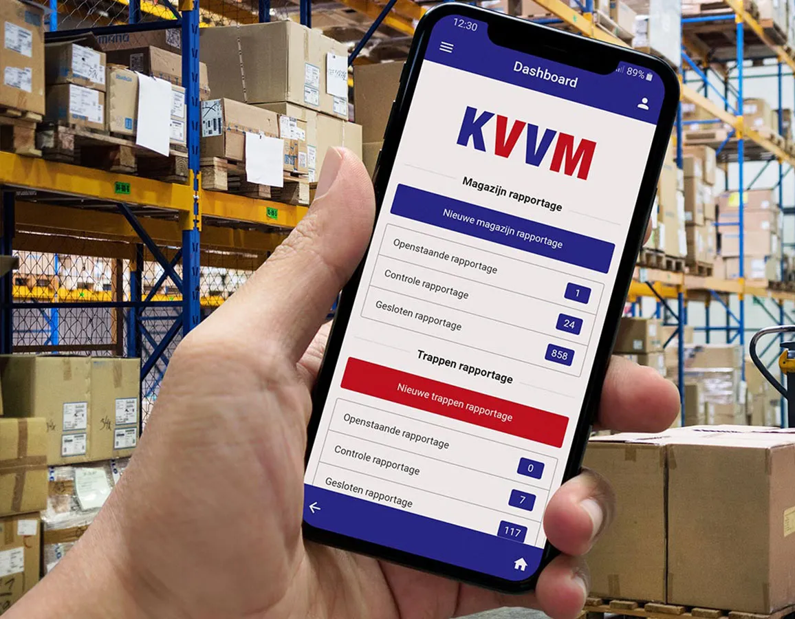 Smartphonebeeld met KVVM-app voor magazijn- en traprapportages, vastgehouden in een magazijn met gestapelde dozen.