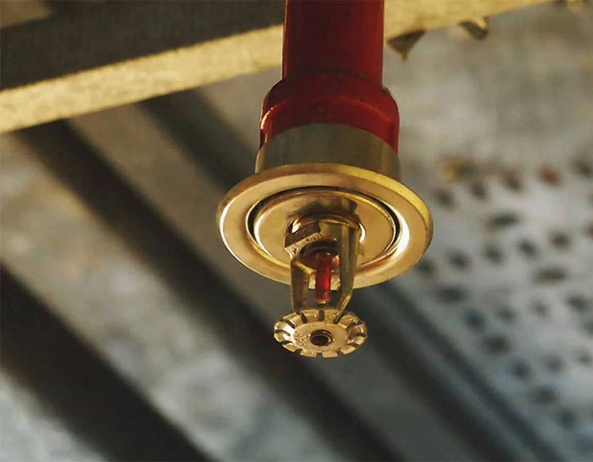 Close-up van een brandsproeier bevestigd aan het plafond van een industrieel gebouw.